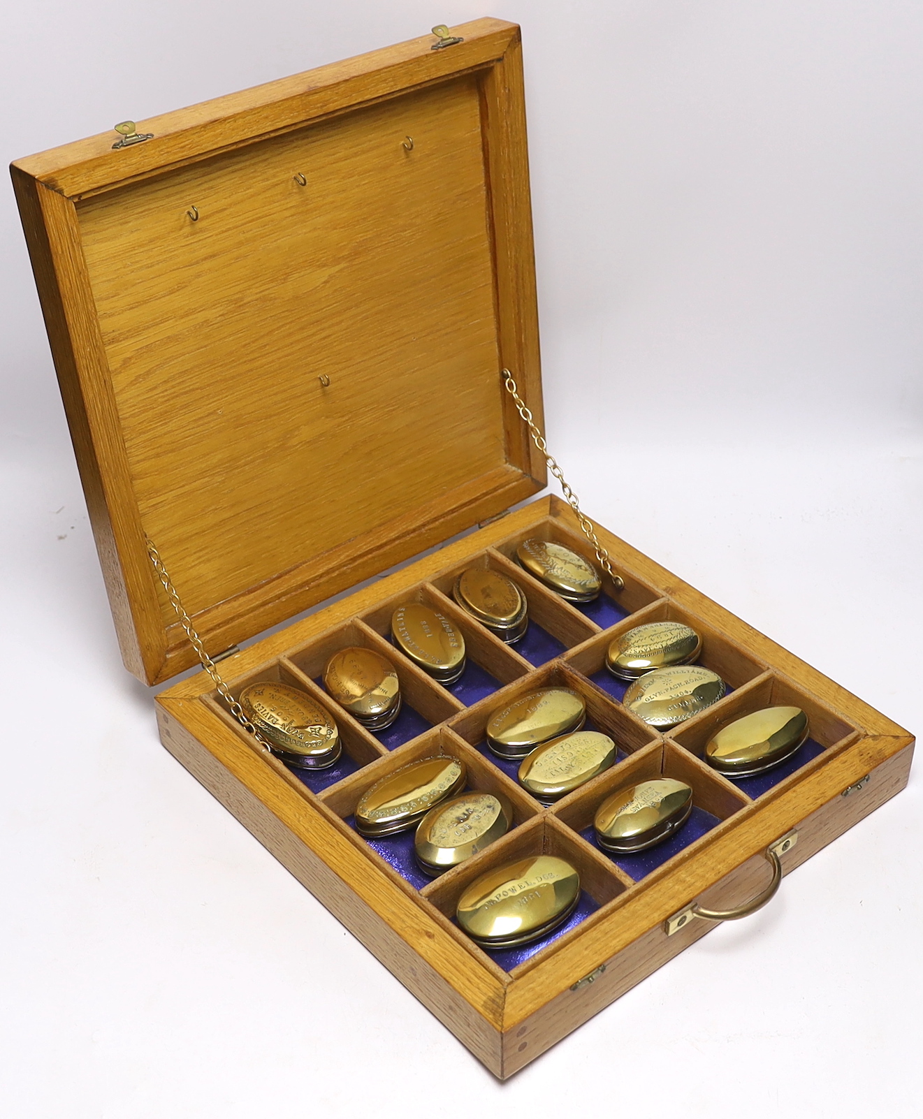 A collection of late 19th and early 20th century Welsh and English miner’s oval brass snuff boxes, most engraved with owner’s name and date, in a sectional oak box, largest snuff box 8cm wide